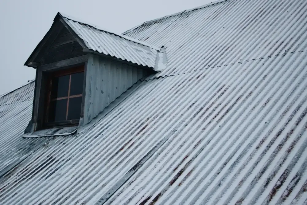 Metal roof with light snow, featuring a dormer window with a wooden frame and frosted glass