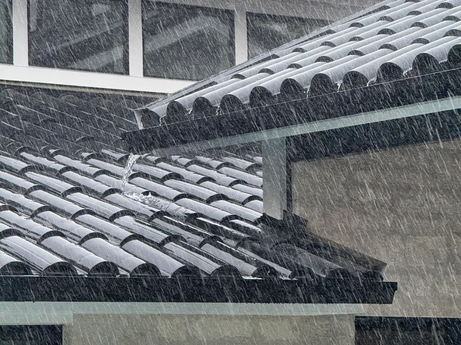 Heavy rain sheeting off a tile roof into the gutter line on a Central Texas home