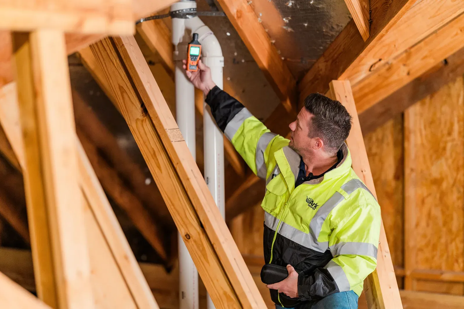 An Ark Roofer inspector taking a moisture reading in an attic among the rafters