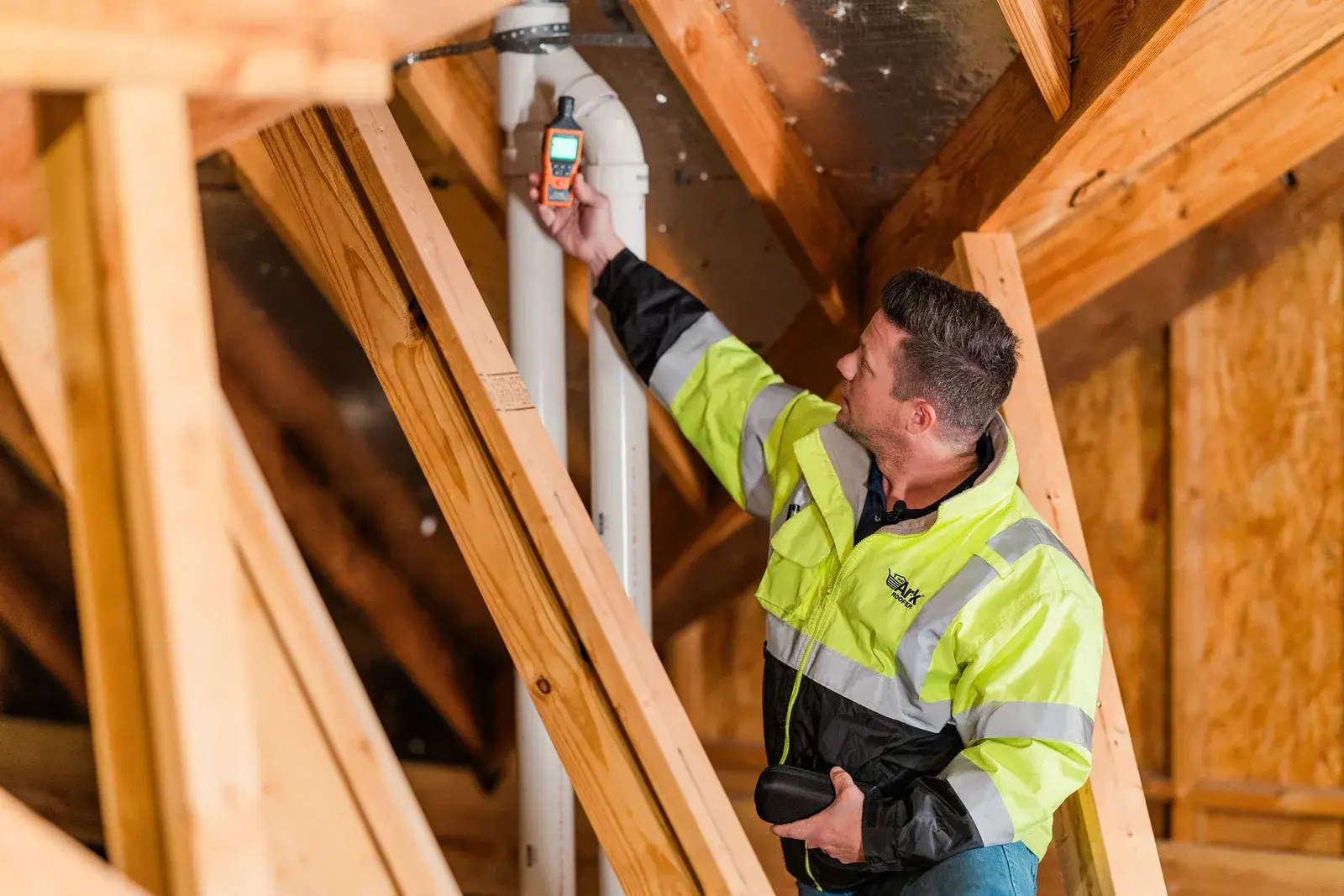 An Ark Roofer inspector taking a moisture reading in an attic among the rafters
