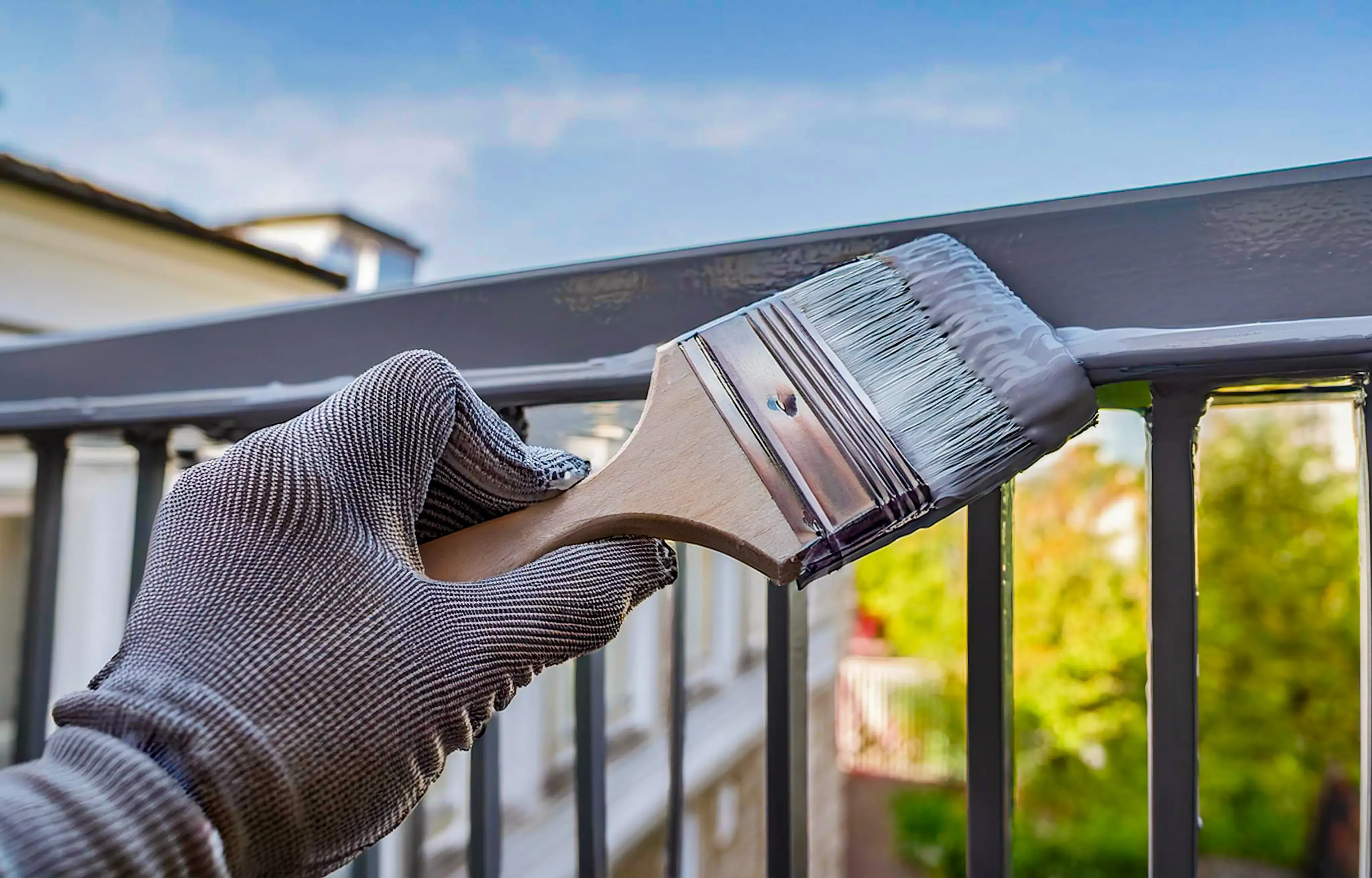 Professional painter applying gray paint to metal balcony railing with precision