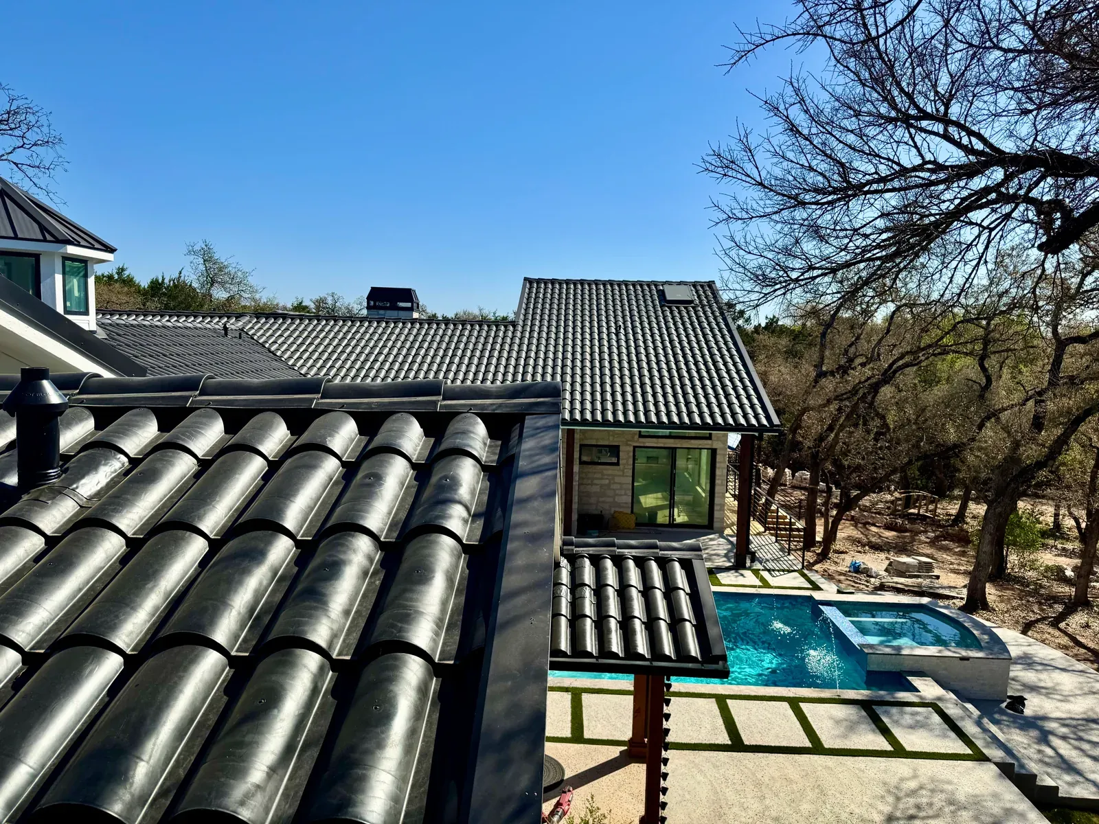Dark steel gutter line holding a crisp profile along a metal tile roof under Central Texas sun