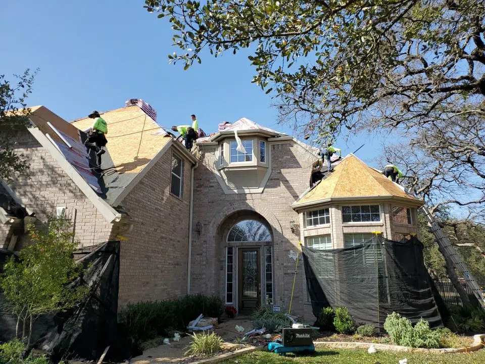 Roofing professionals working on a residential home using ladders and safety gear.