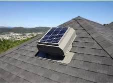 Solar-powered attic fan installed on a shingled roof with a view of the surrounding landscape.