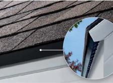 A close-up photo of a roof with a black drip edge and a white fascia board. A portion of the roof shingle is visible in the top left corner.