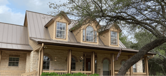 A beige home with a metal roof and a tree in the front yard.