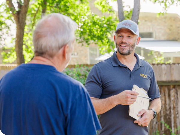 A roofing professional reviewing project plans with a homeowner outside in a backyard, discussing details amidst a tree-filled neighborhood.