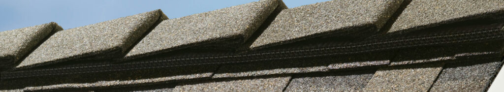 A close-up of a roof with layered shingles installed along the ridge.