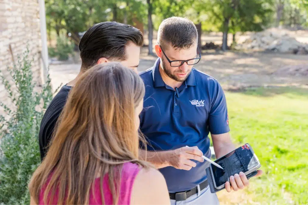 Ark Roofer professional consulting with clients using a tablet in a backyard setting.