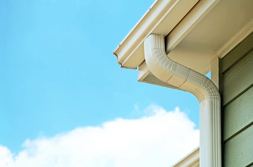 White downspout attached to a residential gutter system against a blue sky.