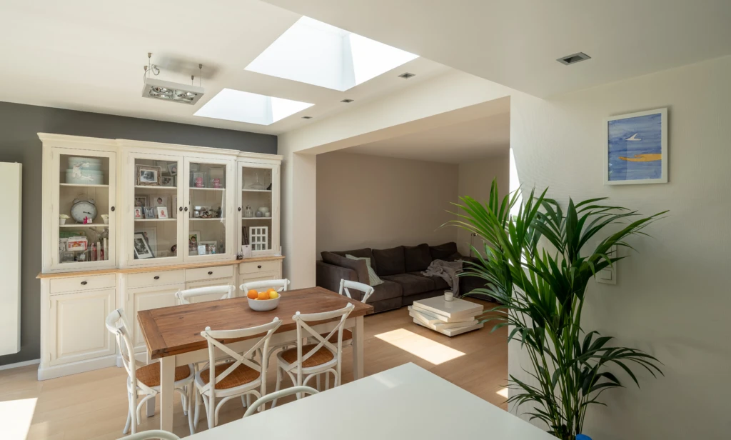 Dining area with a wooden table, white chairs, glass cabinet, and a living room in the background