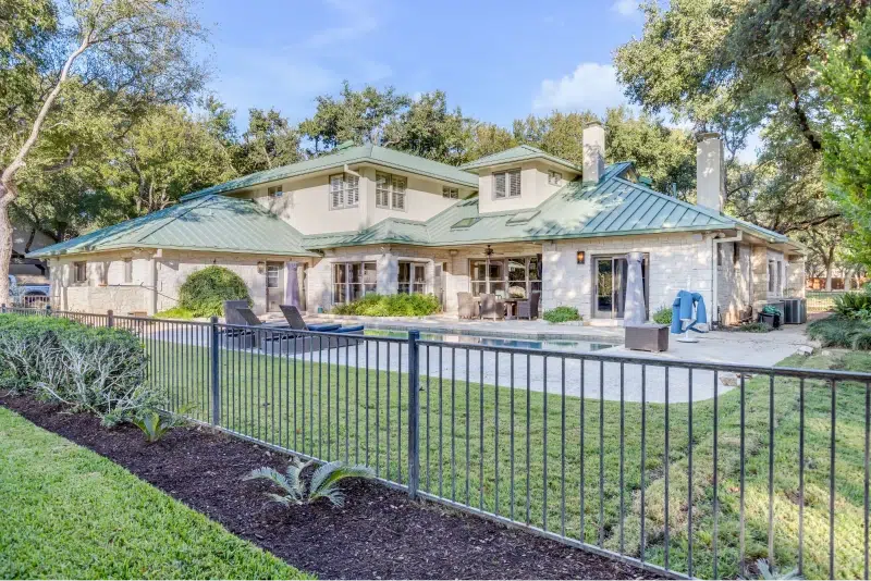 Luxury home with a green metal roof and a spacious backyard with a swimming pool, patio, and well-maintained garden.