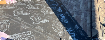 Close-up of roof underlayment with RhinoRoof branding, being installed as part of a roofing project.