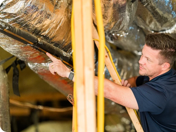 Ark Roofer professional inspecting ductwork and attic ventilation, pointing to a section of insulation.