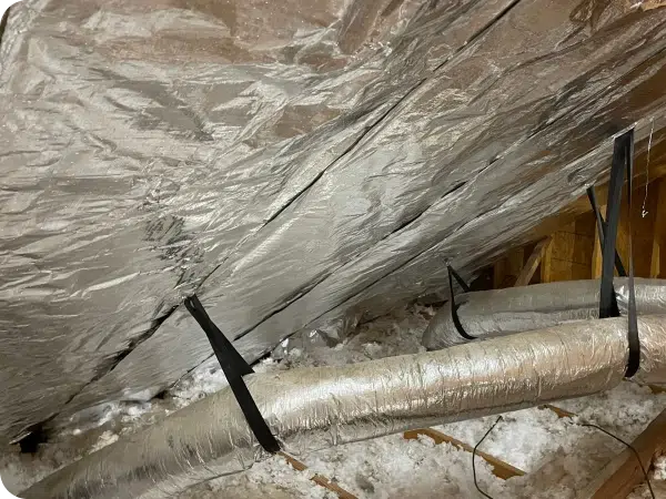 An attic space featuring silver radiant barriers and ventilation ducts.