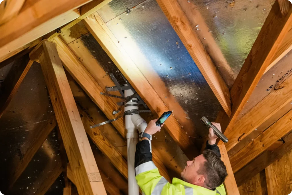 A worker conducting an inspection in the attic using a flashlight.