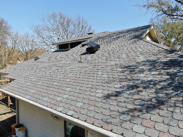 A shingled roof with multiple vents and chimneys under a clear blue sky.