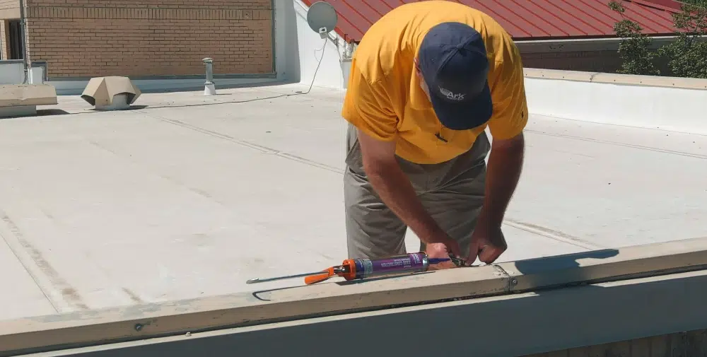 Worker applying sealant to the rooftop edge.