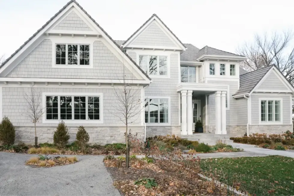 A modern white home with a combination of stone and shingle siding, featuring large windows.