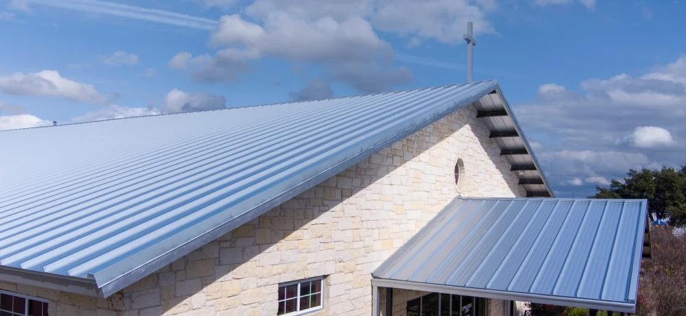 Stone building with a shiny metal roof under a blue sky with scattered clouds