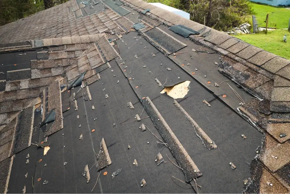 Damaged roof with missing shingles, exposed underlayment, and visible signs of wear and tear