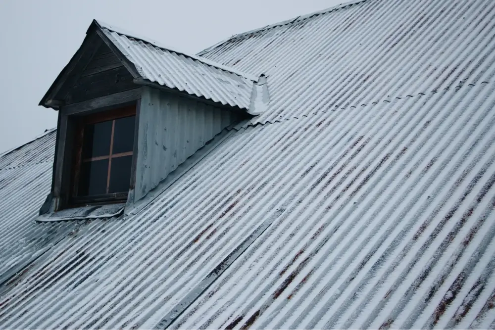 Metal roof with light snow, featuring a dormer window with a wooden frame and frosted glass