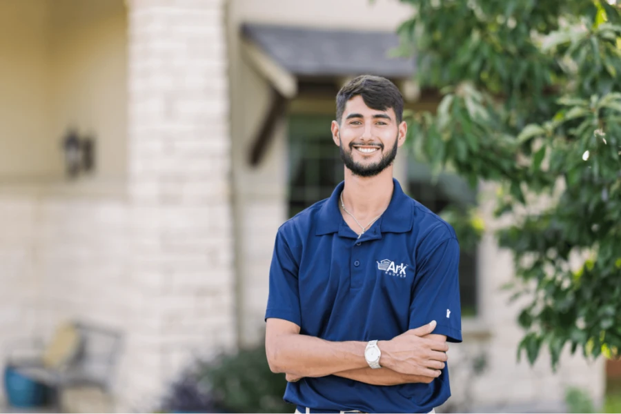 A man smiling, standing outside, wearing a blue Ark Roofing polo shirt.