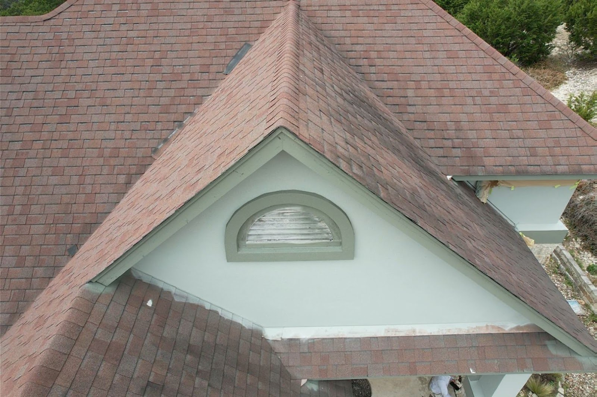 Close-up aerial view of a house roof with red shingles and a circular window vent.