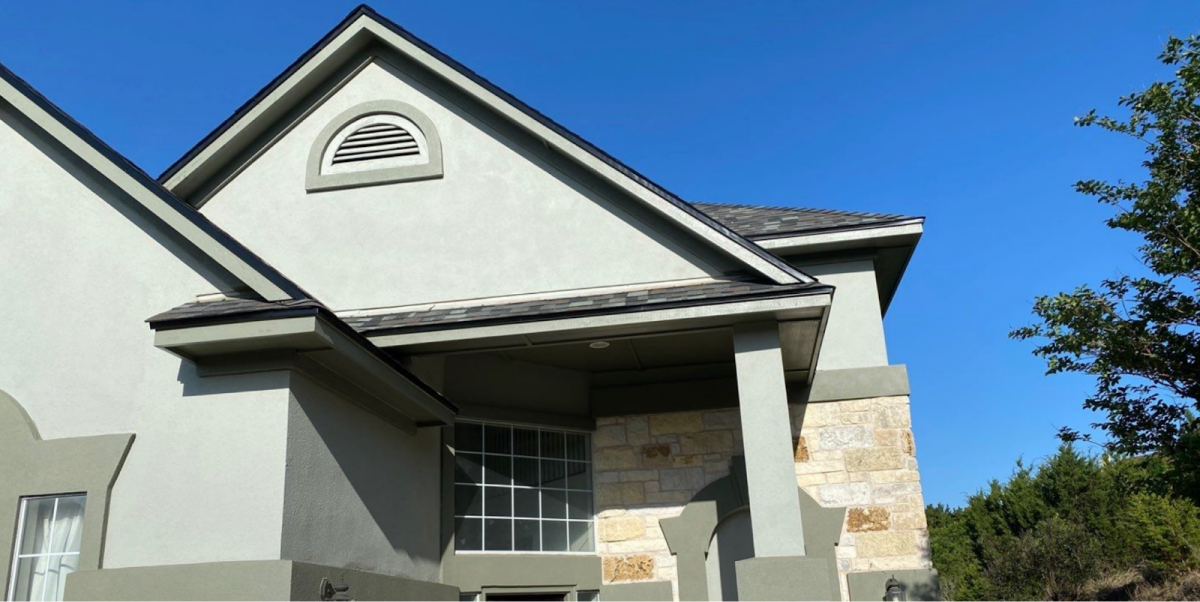 Residential home exterior with a light gray stucco finish and arched window vent.