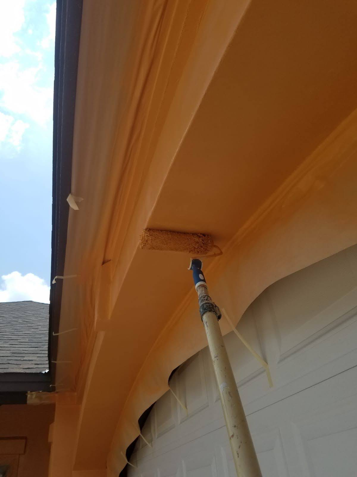 Painting trim above a garage door using a roller brush.