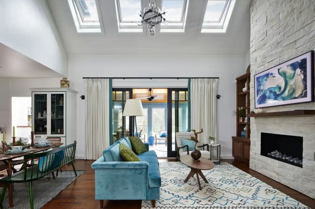 Modern living room interior featuring skylights, a stone fireplace, and stylish decor with a blue sofa and dining area.