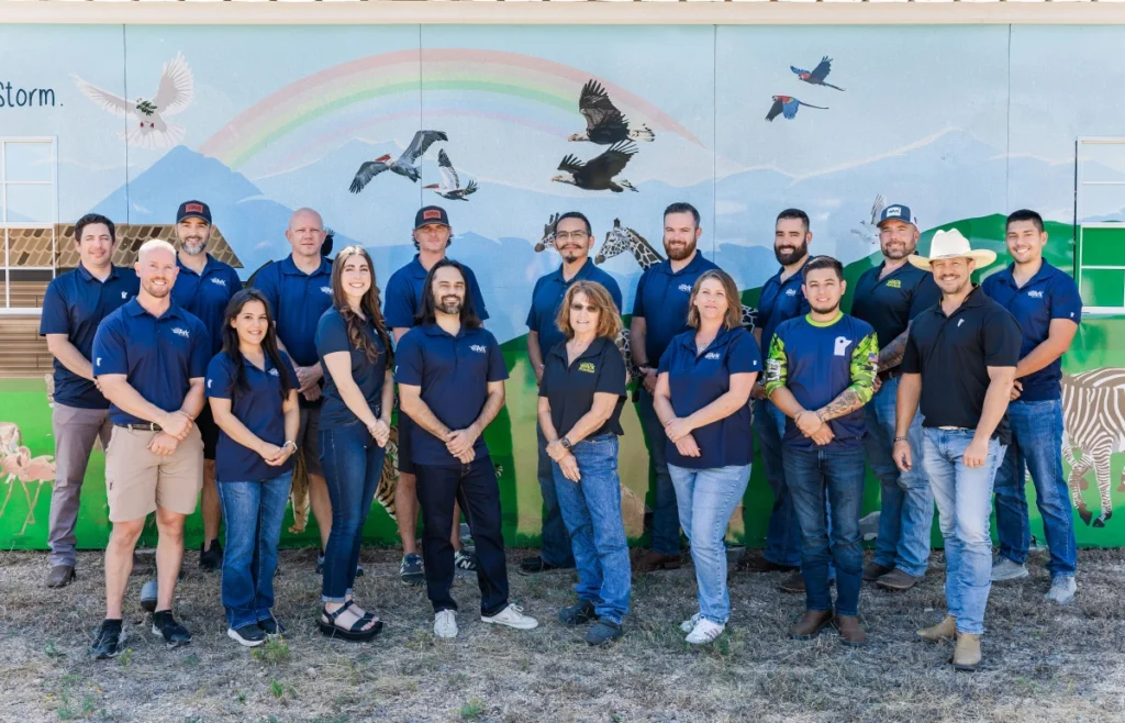 Team photo in front of a mural showcasing Ark Roofer's staff and logo.